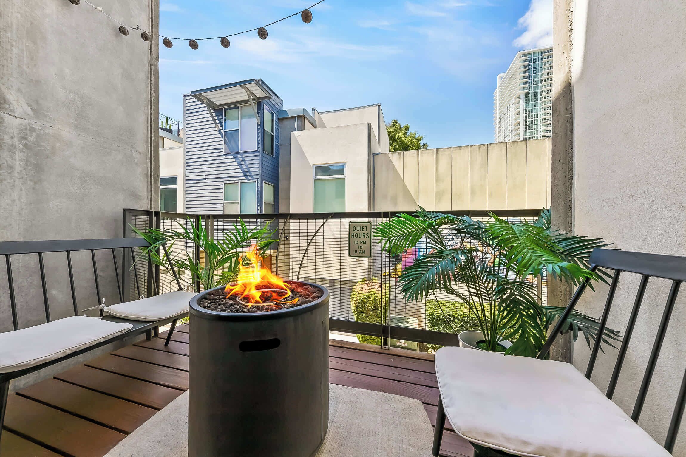 A balcony with a fire pit, seating, and potted plants.