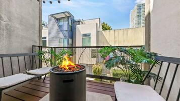 A balcony with a fire pit, seating, and potted plants.