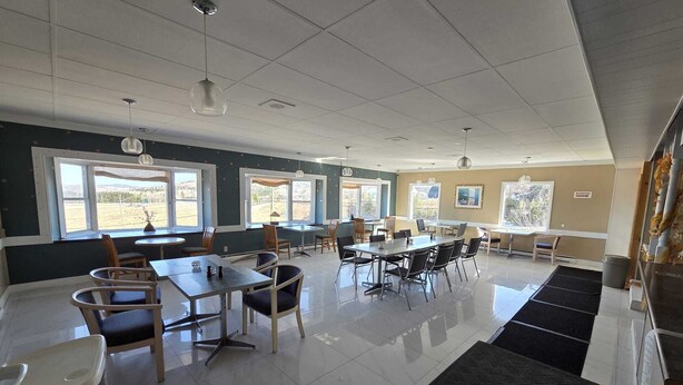 A spacious dining area with multiple tables and chairs, large windows with views, and a clean, tiled floor.