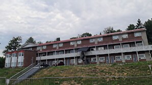 A multi-story building with a red roof, balconies, and a staircase leading to the entrance.