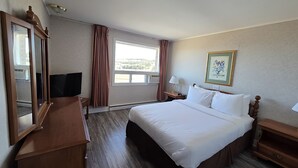 A hotel room with a bed, a dresser, a TV, a window with curtains, and a framed picture on the wall.