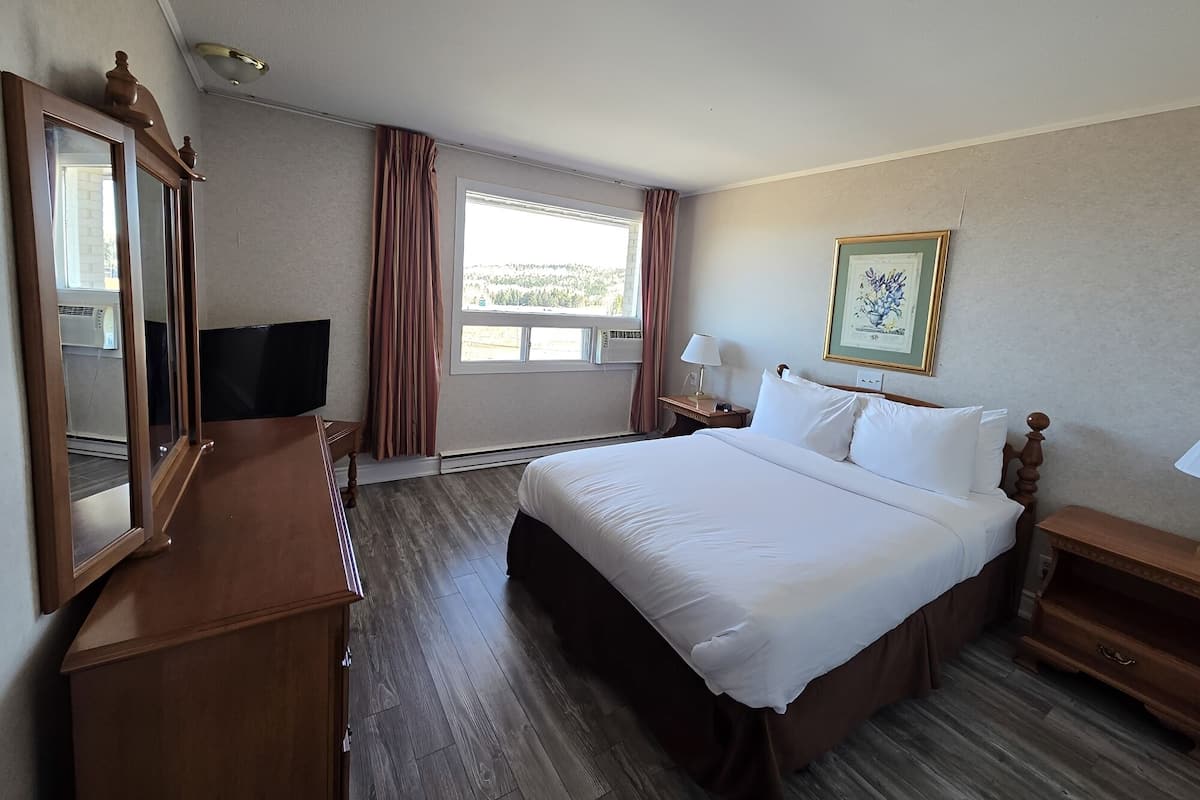 A hotel room with a bed, a dresser, a TV, a window with curtains, and a framed picture on the wall.