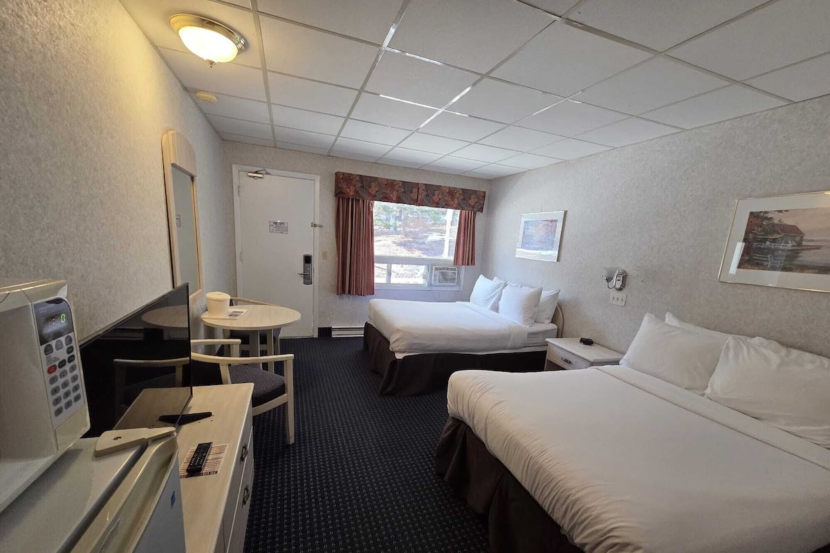 A hotel room with two beds, a desk with a telephone, a microwave, and a small table with a chair.