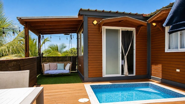 Una terraza de madera con piscina, un columpio y un espacio de estar techado.