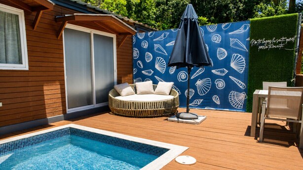 A swimming pool with a wooden deck, a round wicker sofa with cushions, a table and chair, and a blue wall with white shell patterns. - La Ceiba Suite 2  with private plunge pool (Añasco)