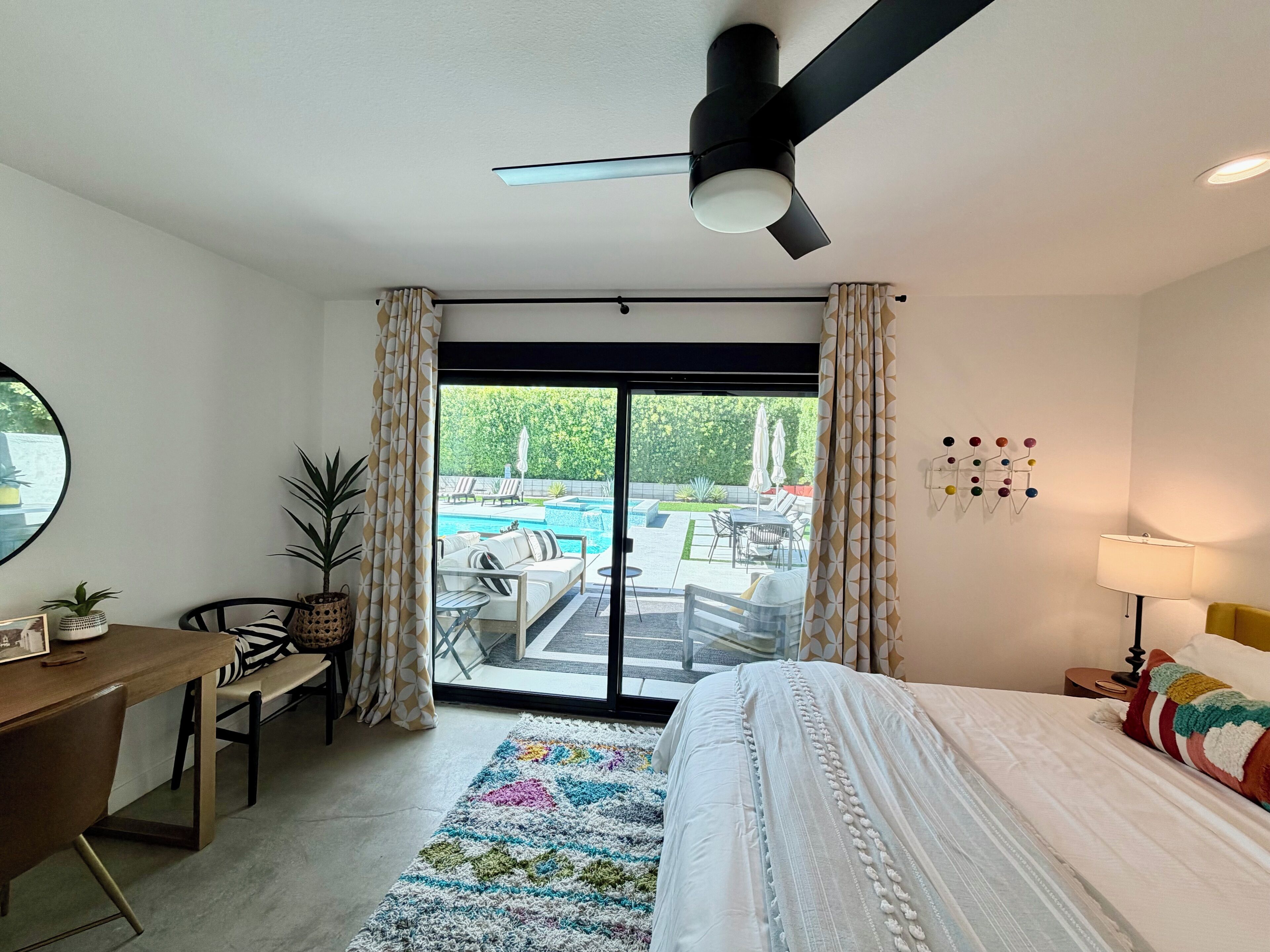 A hotel room with a bed, desk, chair, and a view of an outdoor swimming pool.