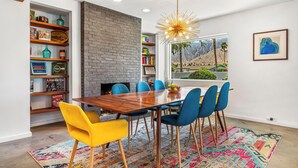 Un comedor con una mesa de madera, sillas azules y amarillas, un tapete colorido y una pared de ladrillo.
