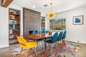 A dining area with a wooden table, blue and yellow chairs, a colorful rug, and a brick wall. - Palm Springs Golden - Your Adventure Awaits! (Palm Springs)