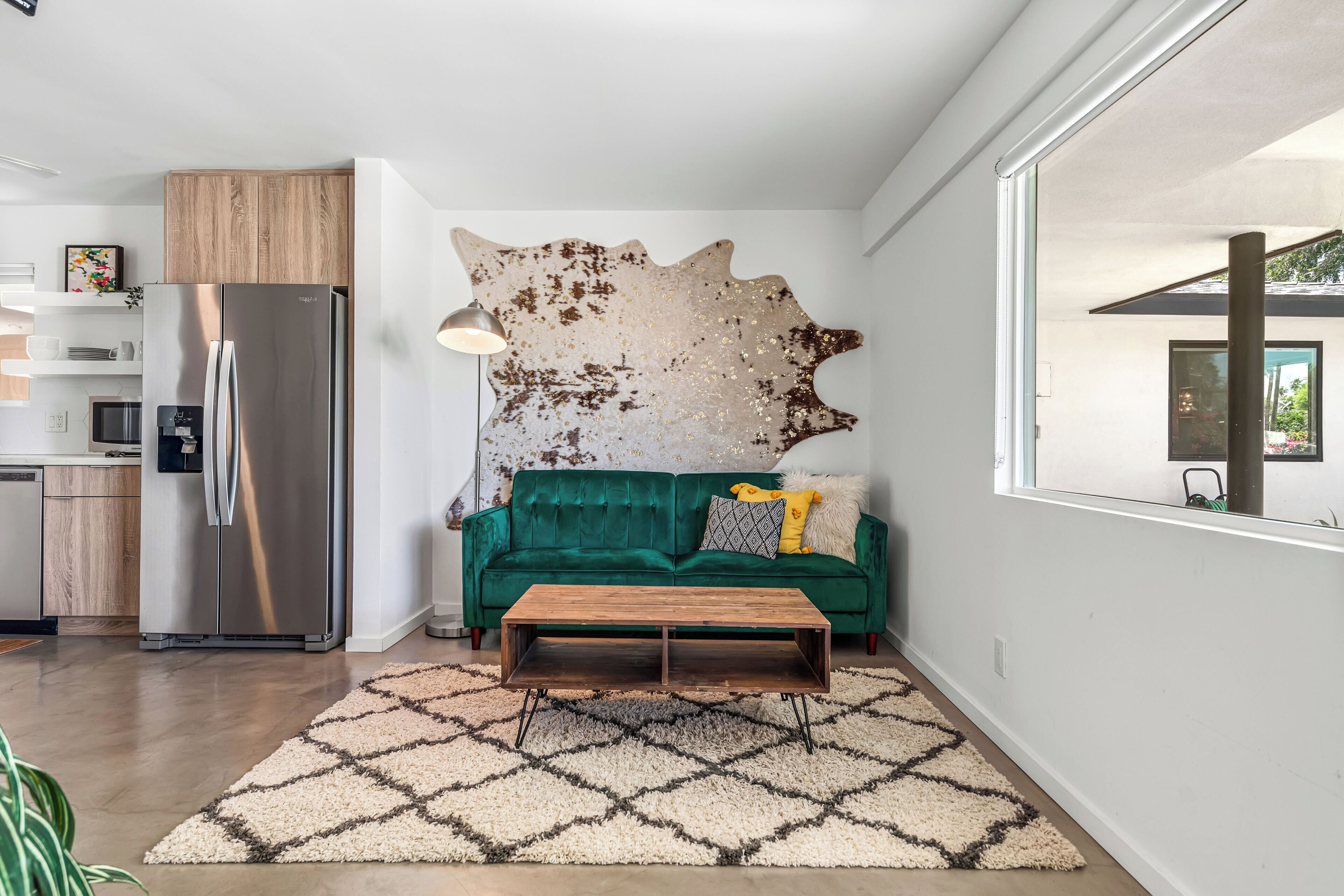 A modern kitchen with a stainless steel refrigerator, a green sofa, and a unique wall art piece.