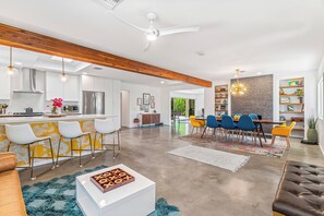 A modern kitchen with white cabinets, a stainless steel refrigerator, and a dining area with a wooden table and blue chairs. - Palm Springs Golden - Your Adventure Awaits! (Palm Springs)