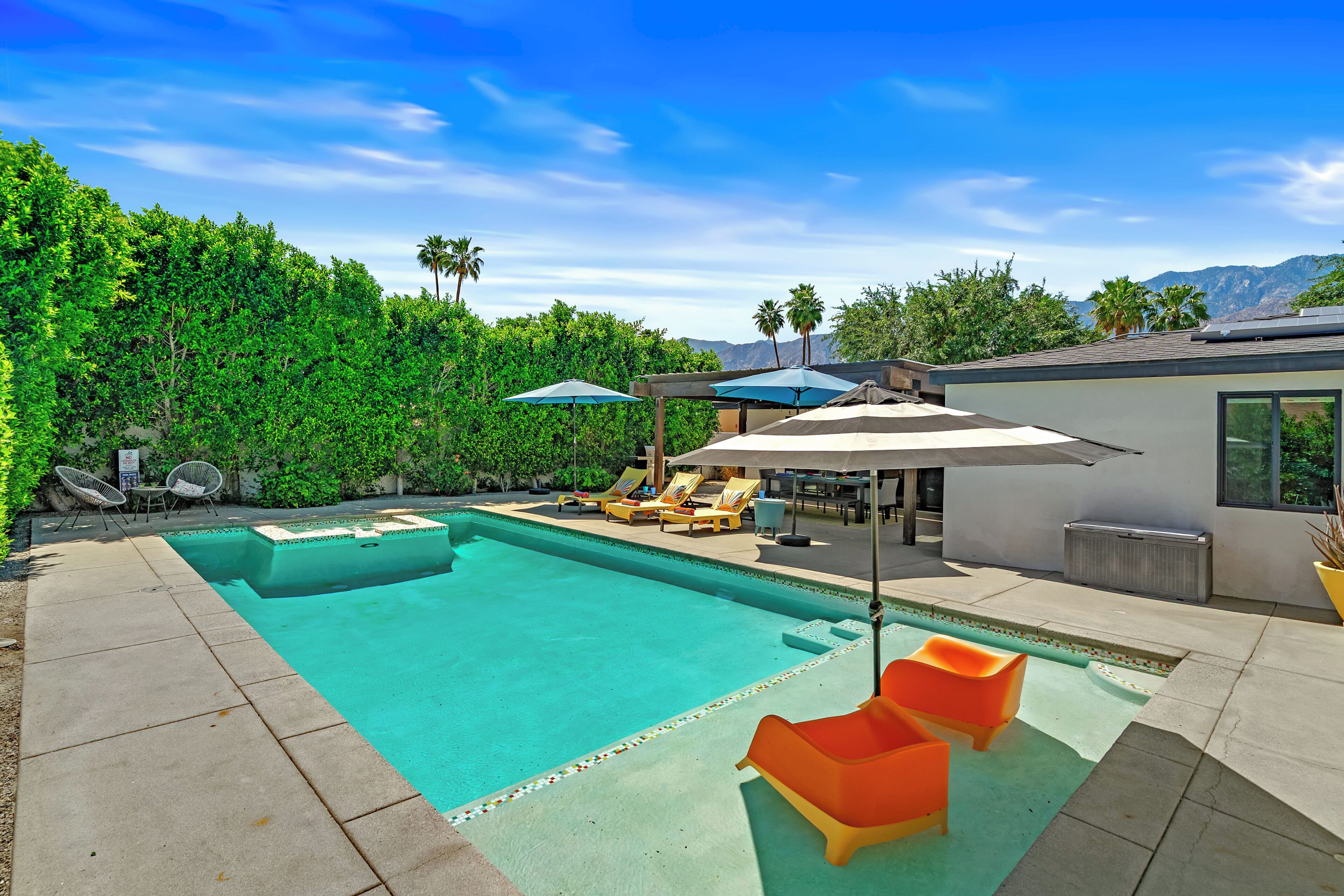 A swimming pool with lounge chairs, a covered seating area, and a view of mountains.