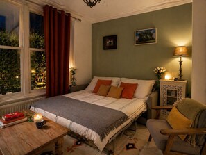 Una camera da letto con un letto, un comodino con libri, una lampada e una sedia.