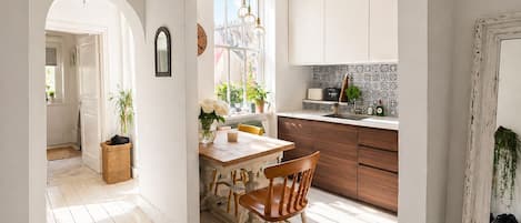 A bright kitchen with wooden cabinets, a dining table with chairs, and a view of the street through a window.