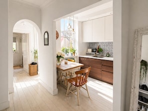 Una cucina luminosa con mobili in legno, un tavolo da pranzo con sedie e vista sulla strada attraverso una finestra.