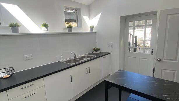 A modern kitchen with white cabinetry, a black countertop, a skylight, and a dining area with a black table and chairs. - High Street House Sleeps 4 with Parking (South Lanarkshire)