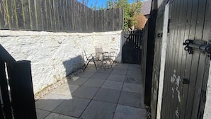 A patio area with a stone wall, a wooden fence, and a gate. - High Street House Sleeps 4 with Parking (South Lanarkshire)