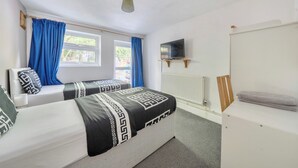 Ein Schlafzimmer mit zwei Betten, einem Fernseher, einem Heizkörper und einem Fenster mit Vorhängen.