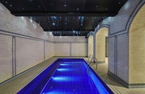 Une piscine dotée d’un plafond étoilé, entourée de murs recouverts de carreaux aux couleurs claires.
