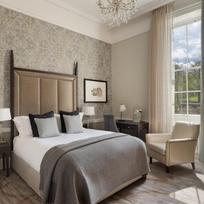 A bedroom with a large bed, a chair, a nightstand, a lamp, and a window with a view. - Ensana Buxton Crescent (Buxton)
