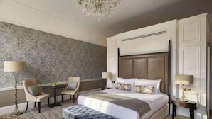 Una habitación de hotel moderna con una cama grande, dos sillas, una mesita y una araña.