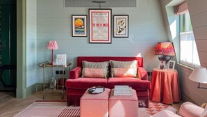 Una sala de estar con un sofá rojo, una mesa de centro, una mesita de noche con una lámpara y cuadros enmarcados en la pared.