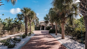 A paved pathway leading to a building with a tiled roof, surrounded by palm trees and other greenery. - Oceanfront Villa w/ Private pool, private oceanfront access & sunset views (Kralendijk)