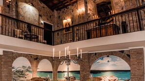 A dining area with a high ceiling, stone walls, and a mural of a beach scene. - Oceanfront Villa w/ Private pool, private oceanfront access & sunset views (Kralendijk)