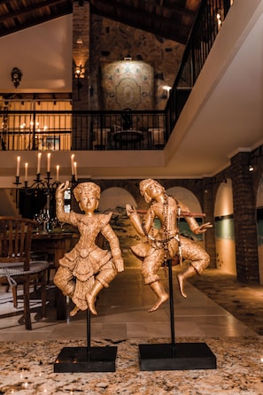 Eine Lobby mit einer Statue einer sitzenden Person auf einem Sockel, einer Chandelüster und einer Treppe.