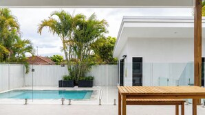 Une maison moderne avec une piscine, une table en bois et une clôture blanche.