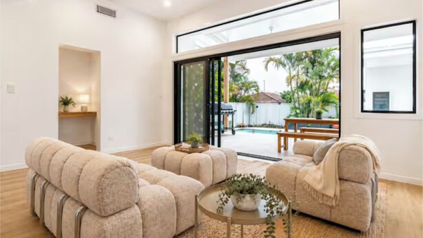 Un salon moderne comprenant un ensemble de canapés, une table basse agrémentée d’une plante, et une porte-fenêtre coulissante donnant sur un espace extérieur avec une piscine et du mobilier de jardin.