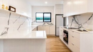 Une cuisine moderne dotée de plans de travail en marbre, d’un four encastré et offrant une vue sur un bâtiment à l’extérieur.