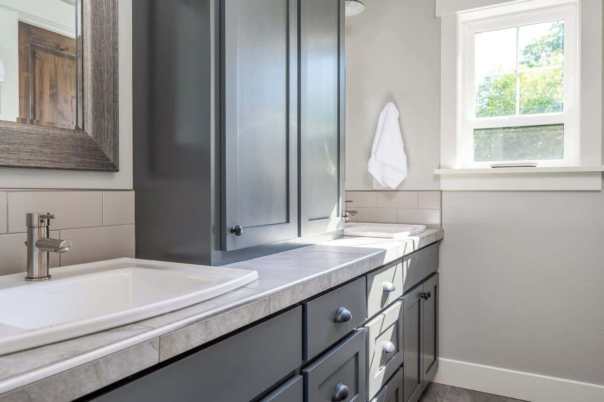 A modern bathroom with a large mirror, two sinks, and a window with a view of greenery.
