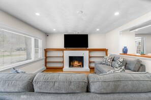 Ein Wohnzimmer mit Kamin, einem Flachbildfernseher und einem grauen Sofa.