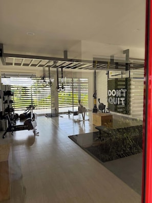 Une salle de sport moderne, dotée de divers appareils d’exercice, de grandes fenêtres et d’une citation motivante sur le mur.