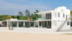 Ein modernes Strandhaus mit Glasfassade, Sitzgelegenheiten im Freien und einer Treppe zum Obergeschoss.