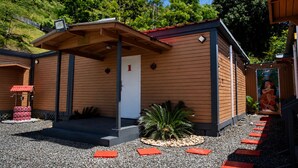 A small, single-story building with a red roof and a white door, surrounded by gravel and plants. - La Palma Suite 1 with outdoor tubs and jacuzzi (Añasco)