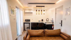 A compact living space with a leather sofa, a kitchenette, a microwave, a refrigerator, and a dining area with two chairs. - La Palma Suite 1 with outdoor tubs and jacuzzi (Añasco)