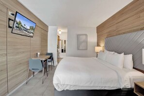 Ein Hotelzimmer mit Bett, Schreibtisch, Stuhl, einem an der Wand montierten Fernseher und Blick ins Freie.