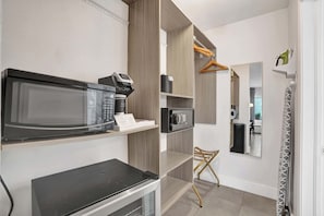 Eine moderne Küche mit Mikrowelle, Kaffeemaschine und kleinem Kühlschrank. Es gibt einen Holzkasten mit einer Kleiderstange und einem Stuhl.
