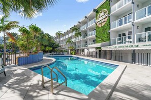 A hotel with a pool, palm trees, and a sign for 'The Greenhouse Terrace Restaurant & Cafe'.