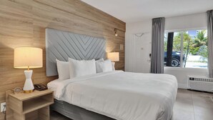 Hotellihuone, jossa on suuri sänky, kaksi yöpöytävalaisinta, puinen sängynpääty, yöpöytä ja näkymä ulos.