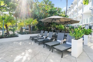 Eine Terrasse mit Lounge-Möbeln, einem großen Sonnenschirm und Kübelpflanzen.