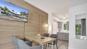 A modern hotel room with a wooden wall, a flat-screen TV, a dining table with chairs, a kitchen area, and a large window. - Ocean Blvd Double Suite with Kitchenette at The Botanica! (Fort Lauderdale)