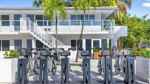 Un edificio moderno con balcón, escalera y una fila de estaciones de carga para bicicletas eléctricas.