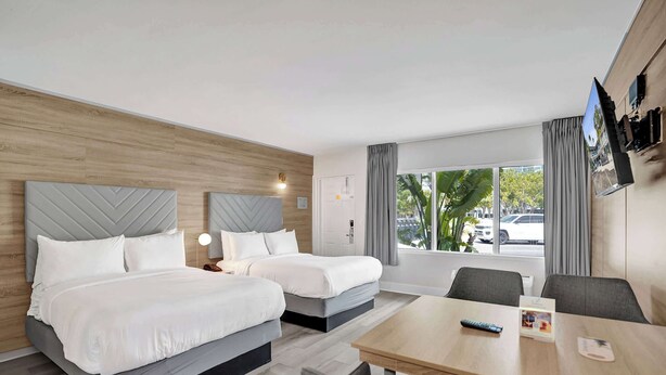 Una habitación de hotel con dos camas, una mesa de comedor y un televisor instalado en la pared.