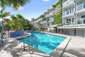 Ein Hotel mit Schwimmbad, Palmen und einem Schild für 'The Greenhouse Terrace Restaurant & Cafe'.