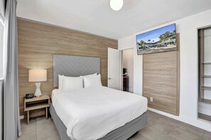 Ein Hotelzimmer mit Bett, Nachttisch mit Lampe, Holz Kopfteil und Blick ins Freie durch ein Fenster.