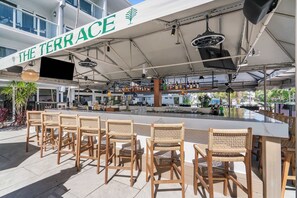 Ein Außenbereich mit Bar, ausgestattet mit weißen Decken, Korbstühlen und einer Bartheke.