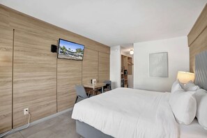 Hotellihuone, jossa on sänky, työpöytä, tuoli, seinälle asennettu televisio ja seinällä oleva kehystetty kuva.