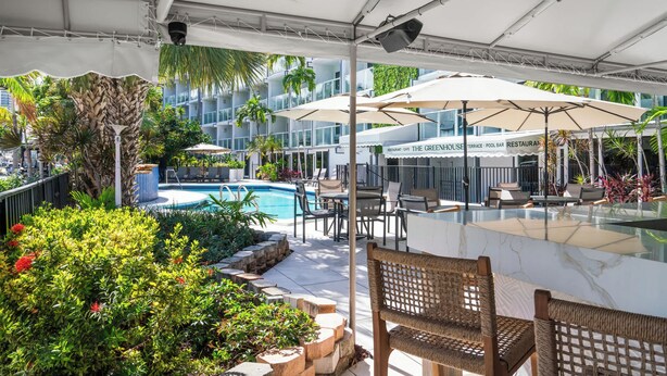 Area piscina all'aperto con lettini, ombrelloni e un ristorante chiamato 'The Greenhouse Terrace Pool Bar'.